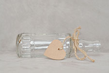 A clear glass bottle with a heart-shaped tag tied to it with twine.