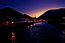 A serene river at dusk with a church steeple in the distance and mountains surrounding it.