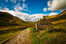An old, abandoned cottage on the side of a dirt road in a picturesque valley