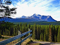 A scenic view of a mountain range with a road and guardrail in the foreground.