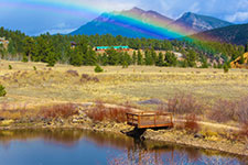 A rainbow stretching over a mountainous terrain with a small body of water in the foreground.