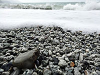 A rocky beach with a wave crashing in the background.