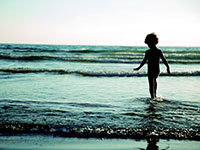 Silhouette of a child standing in shallow ocean water