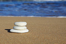 Three white stones stacked on a sandy beach near the ocean