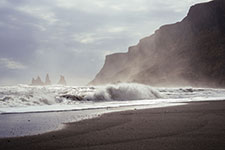 Turbulent waves crashing against a dark sandy beach with rugged cliffs in the background