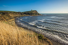A serene coastal scene with a lighthouse on a hill and waves crashing on the shore.