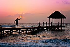 Person releasing a lantern from a wooden dock into the ocean at sunset