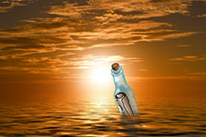 A bottle floating upright in the ocean with the sun setting in the background.