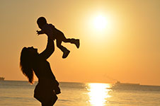 Silhouette of a woman holding a baby in the air against a sunset backdrop at the beach