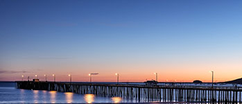 A long pier extending into the ocean at sunset with lights along its length