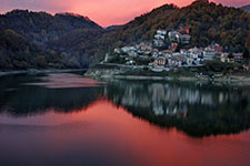 A peaceful village on the lake's edge surrounded by mountains during sunset.