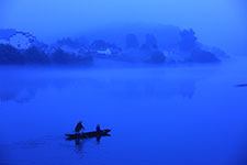 A small boat with two people on a calm lake surrounded by foggy mountains