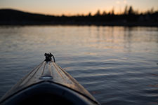 The bow of a kayak on a calm lake at sunset