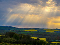 Sunbeams shining through clouds over a green landscape