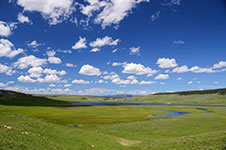 A tranquil landscape with green hills, lakes, and a blue sky dotted with white clouds