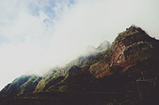 A mountain peak covered in greenery and partially hidden by clouds and mist.