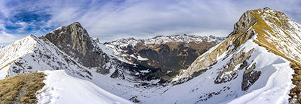 Panoramic view of snow-covered mountains with rugged peaks and a cloudy blue sky.