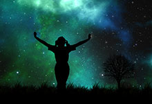 Silhouette of a woman with arms raised towards the starry night sky